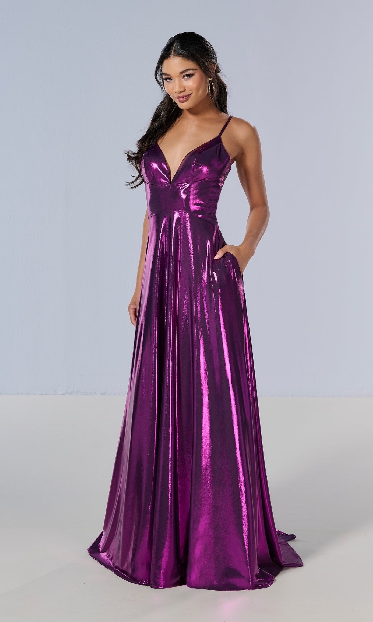 A woman models the Tiffany 16179 long prom dress—a shiny, floor-length purple metallic gown with thin straps and a deep v-neckline—standing against a plain light background.